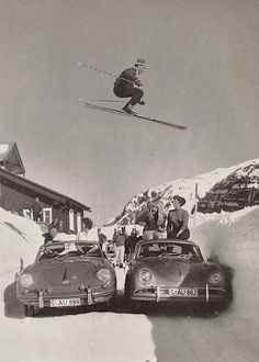 two cars parked on the side of a snow covered road as a person skis over them