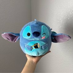 a hand holding up a blue stuffed animal with ears and eyes on it's face