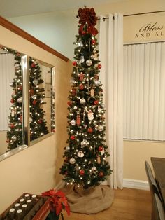 a decorated christmas tree sitting in the corner of a living room next to a mirror