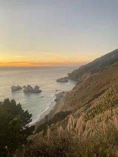 the sun is setting over the ocean and some hills with trees on them in the foreground