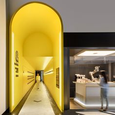 a person walking down a long hallway in a building with yellow lighting on the walls