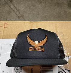 a black trucker hat with an eagle patch sits on top of a cardboard box