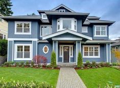 a blue house with lots of windows and landscaping in the front yard, along with green grass