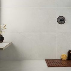 a white tiled bathroom with a wooden tray on the floor next to a shower head and soap dispenser