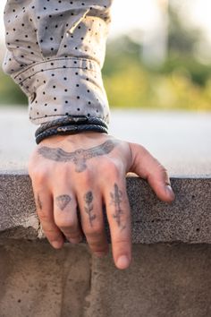 a person's hand with tattoos on it, leaning up against a stone wall