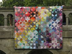 a woman holding up a quilt on top of a stone bridge