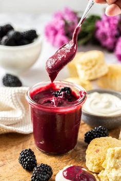 a spoon full of berries and cream being drizzled into a jar filled with jam