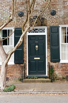 a brick building with black shutters and two trees on the sidewalk in front of it