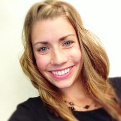 a close up of a person with long hair smiling at the camera and holding a cell phone in her hand