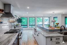 a kitchen with marble counter tops and stainless steel appliances in front of two large windows