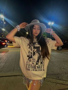 a woman wearing a white hat and t - shirt standing on the street at night