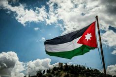 a flag flying in the wind on top of a hill under a cloudy blue sky