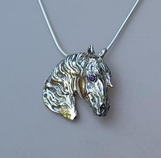 a silver necklace with a horse head on it's back and purple eyes in the center