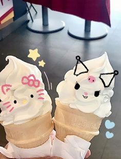 two ice cream cones with hello kitty faces on them are being held up by someone's hand