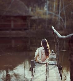 a woman sitting on top of a dock next to a birdcage in the water