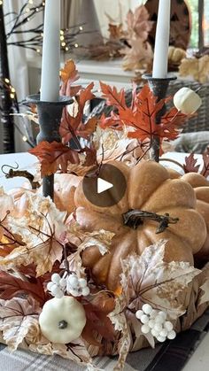 an arrangement of pumpkins, leaves and candles on a table