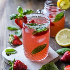 two glasses filled with pink lemonade and strawberries on top of a cutting board