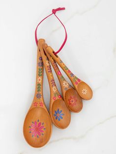 four wooden spoons with designs on them hanging from a red string against a white marble surface