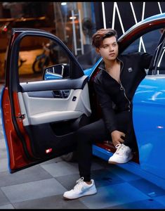 a man sitting in the door of a blue car with his hand on the open door