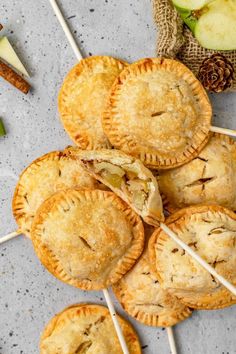 apple pies with toothpicks and apples in the background on a gray surface