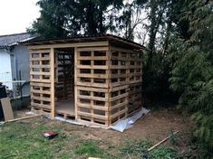 a building made out of wooden pallets sitting in the middle of a yard next to trees