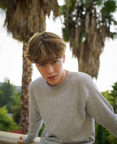 a young boy is leaning on a rail with his hand on his hip and looking at the camera