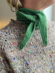 a woman wearing a green knitted bow neck scarf on top of her sweater is looking off to the side