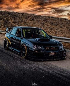 a black car parked on the side of a road next to a hill at sunset