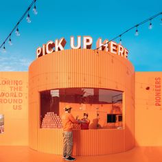 a man standing in front of a store with orange walls and string lights hanging from the ceiling