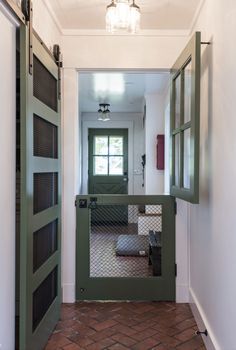 an open door leading to a hallway with green doors and brick flooring on both sides