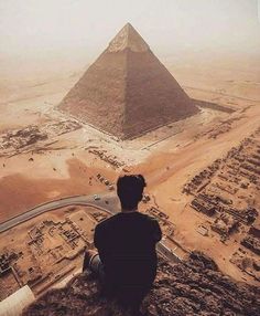 a man sitting on top of a rock next to a large pyramid in the desert