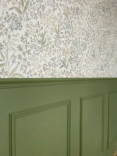 a room with green paneled walls and floral wall paper on the wall behind it