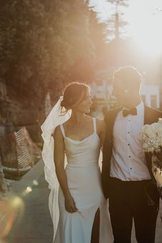 a bride and groom walking down the street at their wedding day, with the sun shining on them