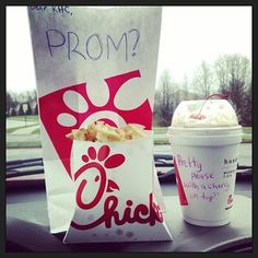 a cup of ice cream next to a paper bag with food in it on the dashboard of a car