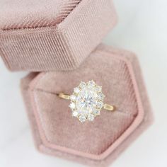 an engagement ring in a pink velvet box with a white diamond center surrounded by smaller round diamonds