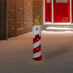 a lighted candy cane in the middle of a snow covered street with red and white doors