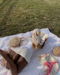 a woman laying on top of a white blanket next to a book and some food