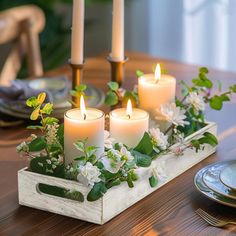 candles are lit on a tray with flowers and greenery