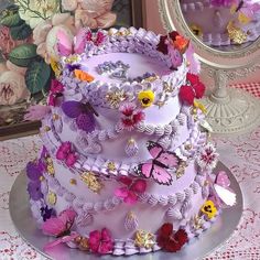 a three tiered cake decorated with flowers and butterflies on a table next to a mirror