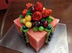 a piece of cake with fruit on it sitting on top of a metal pan covered in watermelon, grapes, kiwis and strawberries