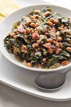 a white bowl filled with beans and greens on top of a plate next to a fork