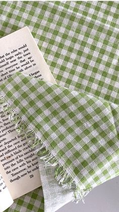 an open book laying on top of a green and white checkered table cloth