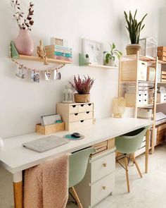 a white desk topped with lots of drawers next to a shelf filled with books and plants