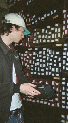 a man standing in front of a wall with lots of boxes on it and wearing a hat