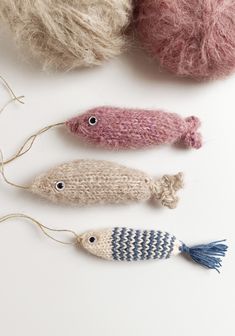 three knitted fish ornaments are shown on a white surface, with yarn balls in the background