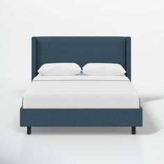 a bed with white pillows and blue upholstered headboard against a white wall