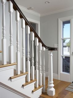 a white staircase with wooden handrails leading up to a large window and door