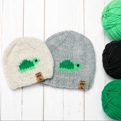 two knitted hats with green and black crochet, one in the shape of a turtle