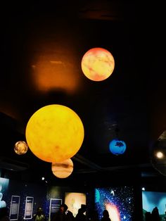 people are looking at the planets on display in a room with black walls and ceiling lights