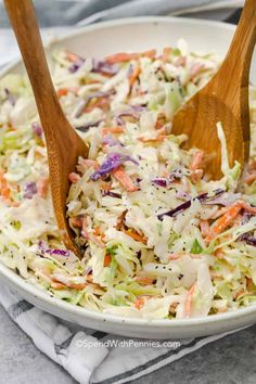 two wooden spoons in a white bowl filled with coleslaw